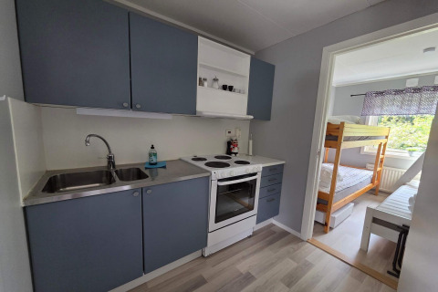 Piccola cucina con mobili blu e forno accanto a una stanza con letto a castello in una baita svedese.