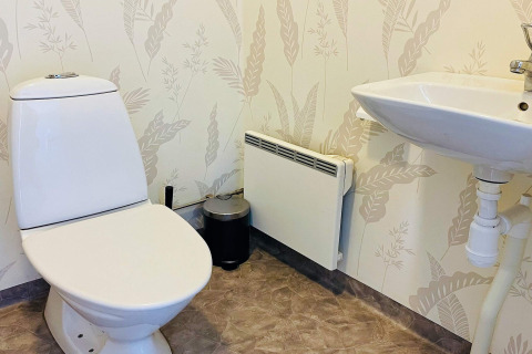 Badkamer met toilet, wastafel en verwarming in een vakantiehuis in Nösund, Zweden, met bladerbehang.