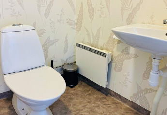 Badkamer met toilet, wasbak en verwarming in een vakantiehuis in Nösund, Zweden, bladerpatroon muur.