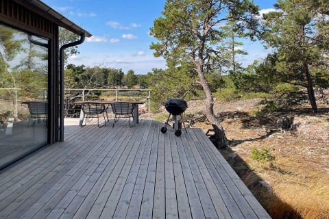Grande terrasse en bois d’une maison de vacances à Väddö, Suède, avec mobilier, barbecue et vue boisée.