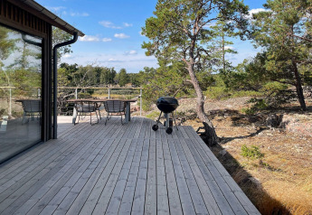 Træterrasse ved en svensk hytte i Väddö med bord, stole og grill omgivet af skov og blå himmel.