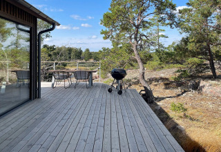 Træterrasse ved en svensk hytte i Väddö med bord, stole og grill omgivet af skov og blå himmel.