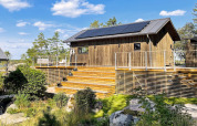 Chalet en bois avec panneaux solaires et grande terrasse à VÄDDÖ, Suède, entouré de nature et ciel bleu.