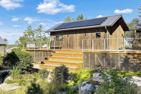 Houten vakantiewoning met zonnepanelen en ruim terras in VÄDDÖ, Zweden, omgeven door natuur en blauwe lucht.