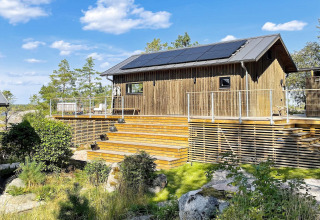 Træhytte med solpaneler på taget, rummelig terrasse og smuk natur i VÄDDÖ, Sverige, under blå himmel.