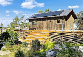 Chalet en bois avec panneaux solaires et grande terrasse à VÄDDÖ, Suède, entouré de nature et ciel bleu.