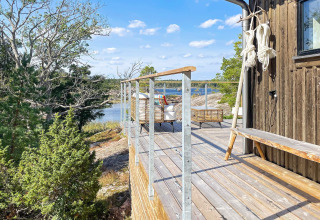 Træterrasse med udsigt over vand og skov ved en hytte i VÄDDÖ, Sverige på en solrig dag.