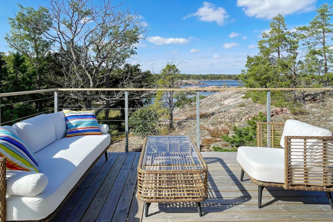 Terraza exterior con muebles de mimbre y cojines coloridos, con vistas a rocas y mar en Väddö, Suecia.