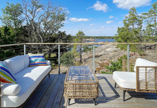 Terrasse extérieure avec meubles en osier et coussins colorés, vue sur rochers et mer à Väddö, Suède.