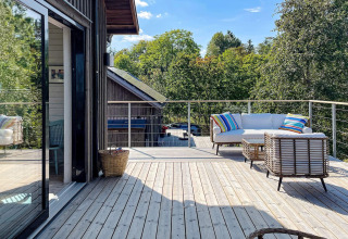 Moderne Terrasse einer Ferienhütte in VÄDDÖ, Schweden, mit Rattansofa und bunten Kissen.