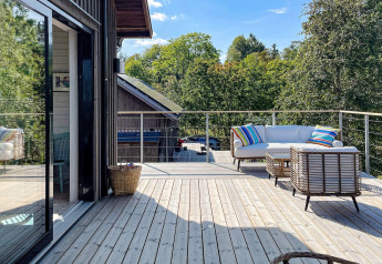 Ruim houten terras aan een vakantiehuis in VÄDDÖ, Zweden, met buitensoFa en kleurrijke kussens.