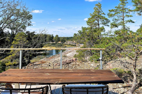 Holztisch mit Stühlen auf Terrasse mit Blick auf Fluss, Felsen und Bäume am 4-Sterne-Ferienhaus in VÄDDÖ, Schweden.