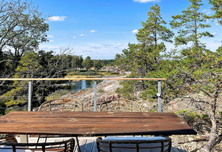 Houten tafel en stoelen op terras met zicht op rivier, rotsen en bos bij 4-sterren vakantiehuis in VÄDDÖ, Zweden.