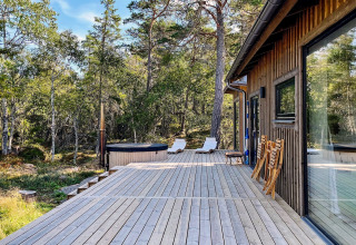 Grande terrasse boisée à la maison de vacances VÄDDÖ, Suède, avec spa, chaises et vue forêt.