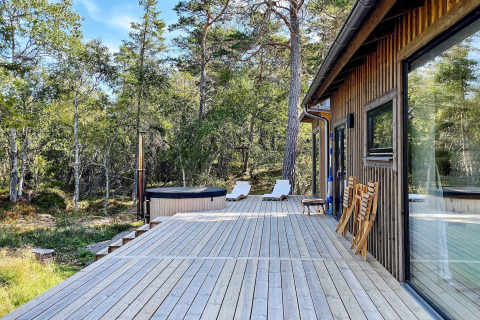 Terrasse eines Ferienhauses in VÄDDÖ, Schweden, mit Hot Tub und Liegestühlen im Wald.
