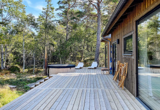 Udendørs terrasse ved feriehus i VÄDDÖ, Sverige, omgivet af skov med liggestole og spabad.