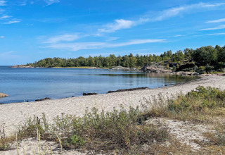Plage de sable sur la côte à Väddö, Suède, avec eau calme, végétation et ciel bleu en arrière-plan.