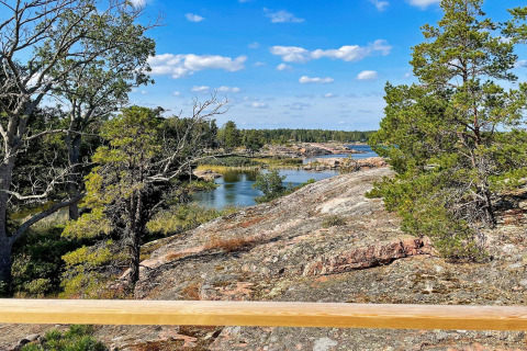Vue d'un chalet à VÄDDÖ, Suède, montrant rochers, arbres et eau sous un ciel bleu clair.