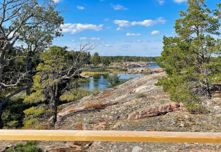 Vista da una baita a VÄDDÖ, Svezia, con rocce, alberi e acqua sotto un cielo azzurro.