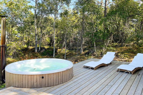Udendørs spabad og liggestole på en træterrasse ved en skov ved kabinen '4 star holiday home in VÄDDÖ', Sverige.