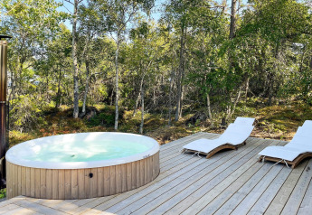Udendørs spabad og liggestole på en træterrasse ved en skov ved kabinen '4 star holiday home in VÄDDÖ', Sverige.