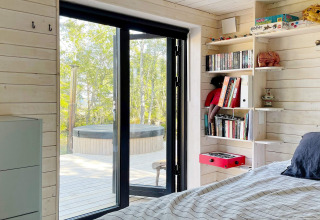 Slaapkamer in een vakantiewoning in Väddö, Zweden met zicht op het terras en buitenspa in het groen.