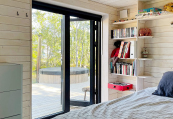 Schlafzimmer in einem Ferienhaus in Väddö, Schweden mit Blick auf Terrasse und Whirlpool im Freien.