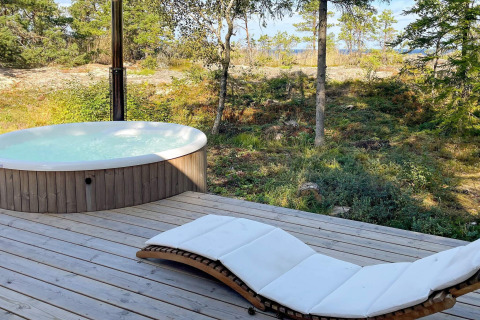 Terraza de madera al aire libre con jacuzzi redondo y tumbona blanca, rodeada de naturaleza sueca en Väddö.