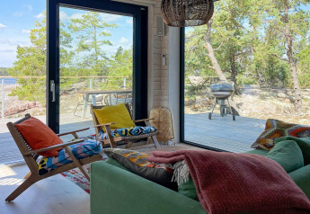 Salón en casa de vacaciones en VÄDDÖ, Suecia, con cojines coloridos, grandes ventanales y vista a terraza.