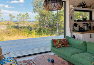 Salon chaleureux d'un gîte 4 étoiles à VÄDDÖ, Suède, avec canapé vert et vue sur la nature extérieure.
