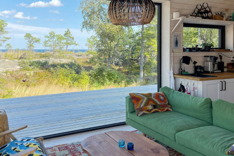 Gemütliches Wohnzimmer in einem Ferienhaus in VÄDDÖ, Schweden, mit grünem Sofa und Naturblick.