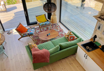 Lichte woonkamer in een Zweedse cabin met groene bank, kleurrijke kussens en grote glazen deuren naar het terras.