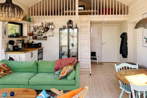 Intérieur chaleureux d'un chalet à VÄDDÖ, Suède, avec canapé vert, cuisine et mezzanine.