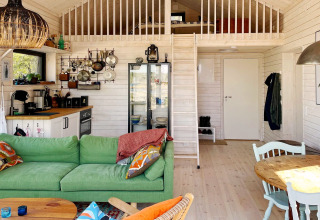 Intérieur chaleureux d'un chalet à VÄDDÖ, Suède, avec canapé vert, cuisine et mezzanine.