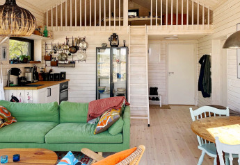 Intérieur chaleureux d'un chalet à VÄDDÖ, Suède, avec canapé vert, cuisine et mezzanine.