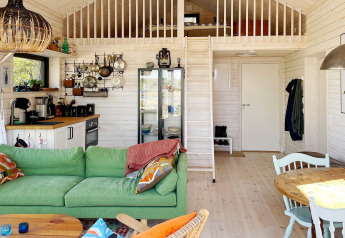 Intérieur chaleureux d'un chalet à VÄDDÖ, Suède, avec canapé vert, cuisine et mezzanine.