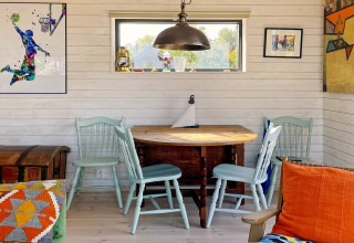 Coin lumineux et chaleureux dans un chalet suédois, avec chaises bleues, table en bois et œuvres colorées.