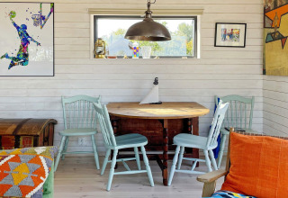 Coin lumineux et chaleureux dans un chalet suédois, avec chaises bleues, table en bois et œuvres colorées.