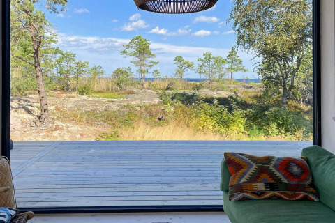 Vue d’un chalet à VÄDDÖ, Suède, avec terrasse en bois et nature verdoyante sous un ciel bleu.