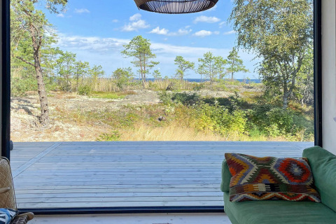 Vue d’un chalet à VÄDDÖ, Suède, avec terrasse en bois et nature verdoyante sous un ciel bleu.
