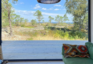 Vista desde una cabaña en VÄDDÖ, Suecia, con terraza de madera, sillón verde y hermoso paisaje natural.