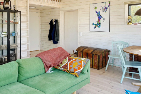 Knusse woonkamer in een vakantiehuis met groene zetel, kleurrijke kunst, antieke kist en houten muren in VÄDDÖ, Zweden.