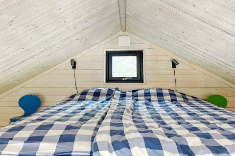 Slaapkamer in een hut in VÄDDÖ, Zweden, met een schuin plafond, geruit beddengoed en kleine tafels.