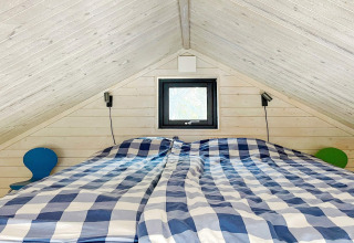 Chambre d'une cabane à VÄDDÖ, Suède, plafond en pente, linge de lit à carreaux bleu et tables basses.