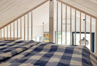 Blick vom Schlafbereich im Loft eines charmanten Ferienhauses in VÄDDÖ, Schweden, mit Karobettwäsche.