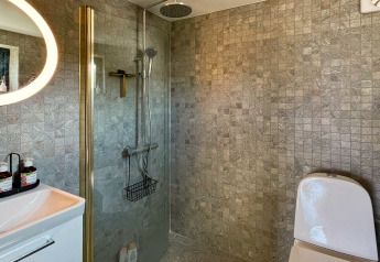 Moderne badeværelse i en hytte i VÄDDÖ, Sverige med bruser, toilet og stilfulde klinkevægge.