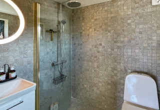 Modernes Badezimmer in einer Ferienhütte in VÄDDÖ, Schweden, mit Dusche, Toilette und Fliesenwänden.