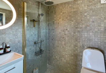 Salle de bain moderne dans une maison de vacances à VÄDDÖ, Suède, avec douche, toilettes et murs carrelés.