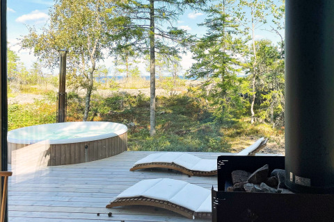 Vue depuis le chalet à VÄDDÖ, Suède, avec jacuzzi extérieur, chaises longues et forêt verdoyante.