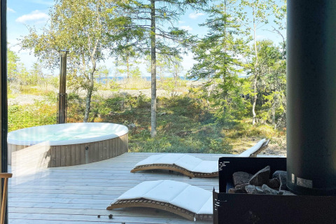 Vue depuis le chalet à VÄDDÖ, Suède, avec jacuzzi extérieur, chaises longues et forêt verdoyante.